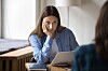 Woman in blue shirt listening during a job interview at a table with a laptop.