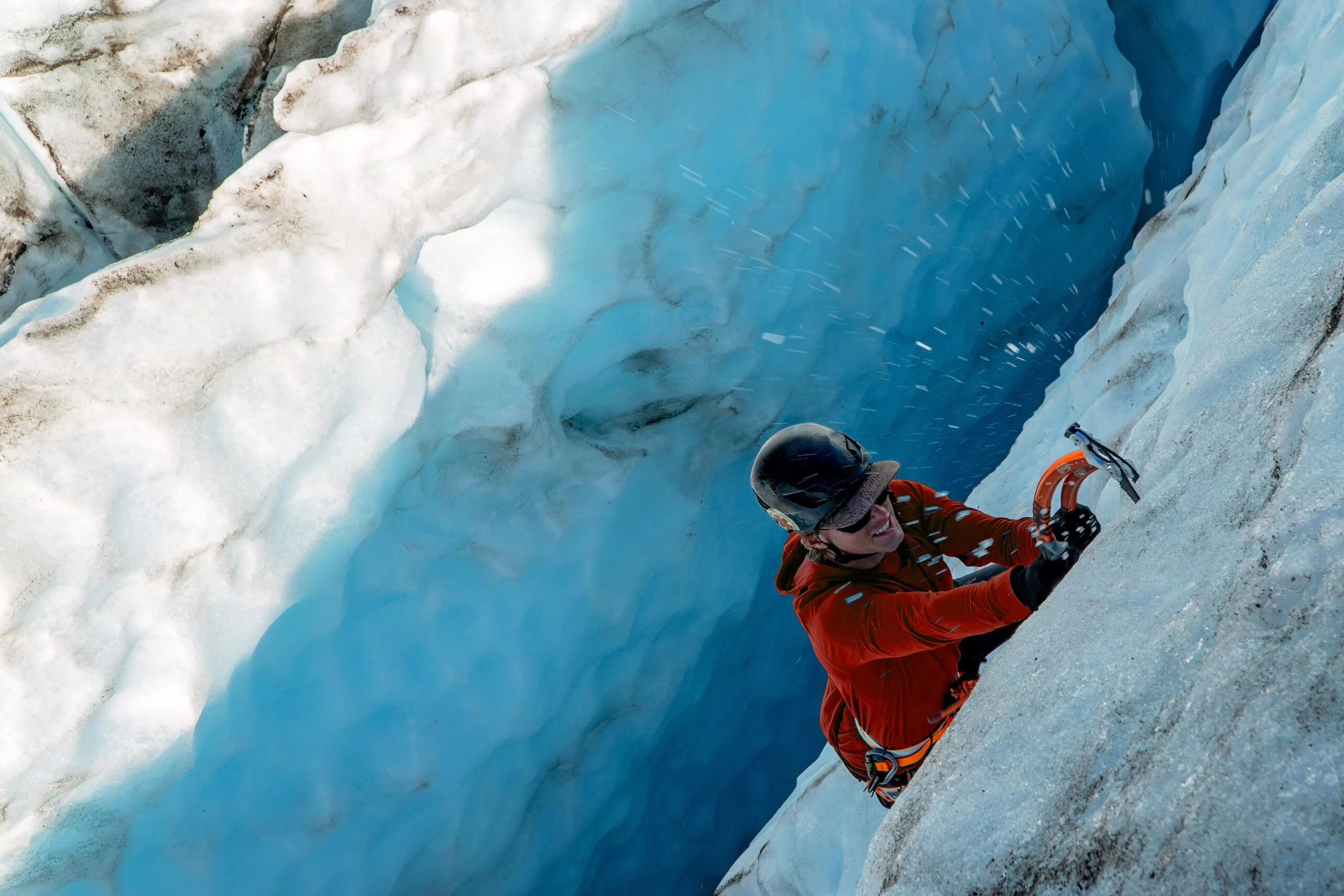 A climber on the Alpine Ice Introduction course swings their ice axe into blue alpine ice.