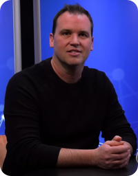 Man in dark shirt onstage faces camera
