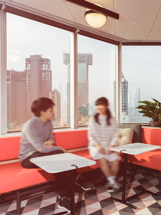 Duas pessoas sentadas em um sofá vermelho em frente à janela.
